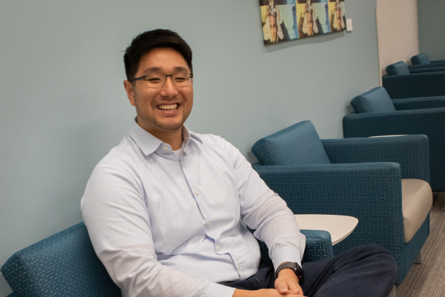 Peter Hsiue sitting on a chair in a waiting room, smiling and looking at the camera