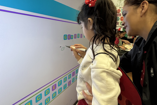 A woman shows a young child how to draw with a marker on a board.