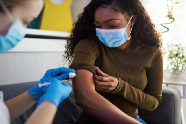 Person receiving an injection in the upper arm from a healthcare professional wearing blue gloves.