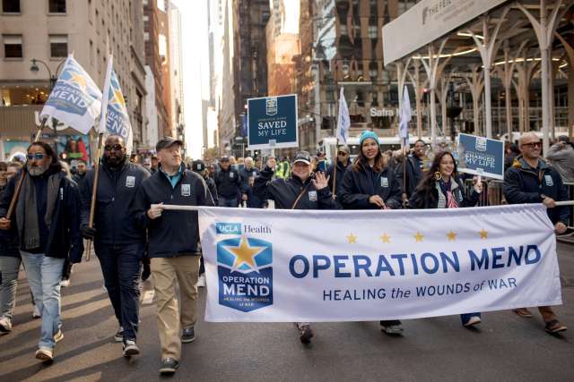 Participants march in the Operation Mend parade, holding banners and flags.