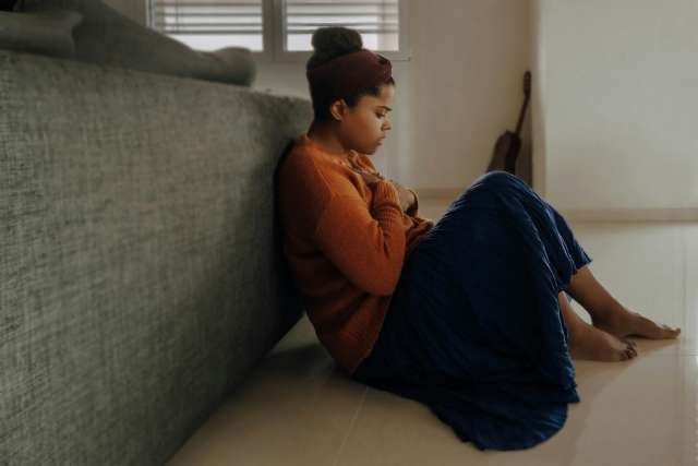 A depressed younger woman sits against her bed.