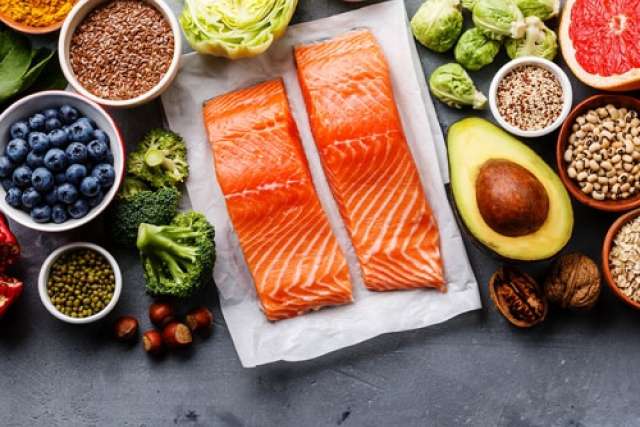 Two raw salmon fillets surrounded by various healthy foods like blueberries, avocado, broccoli, grapefruit, and nuts, arranged on a gray surface.