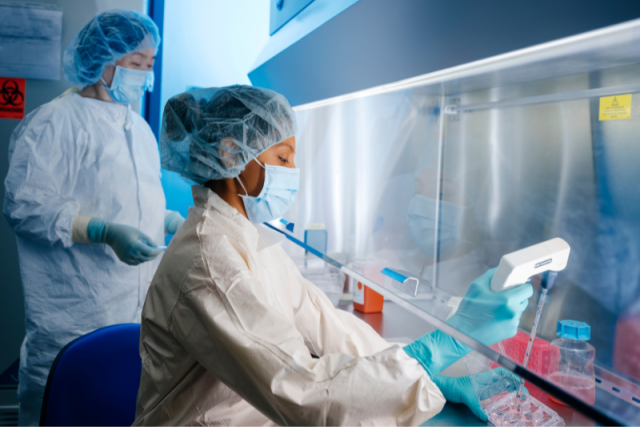 Two scientists covered in PPE work at a UCLA cell therapy lab station.