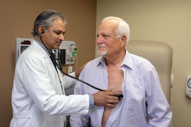  Dr. Ravi Dave listening to older man's chest with a stethoscope in an exam room
