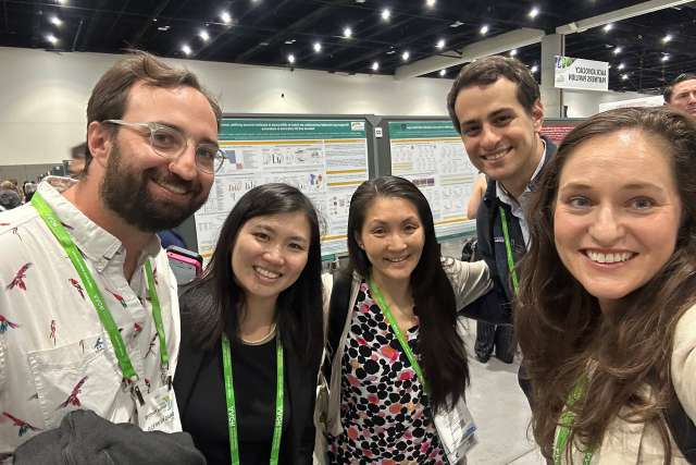 Five conference attendees smiling in front of a research poster