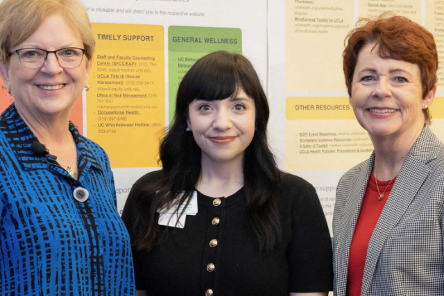 Three women standing together in front of a presentation poster.