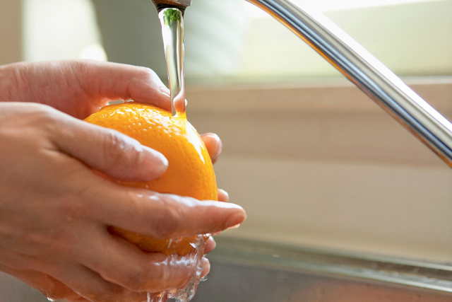 A person washes an orange in the kitchen sink