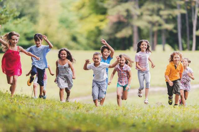 Group of smiling children running toward the camera in a grass field