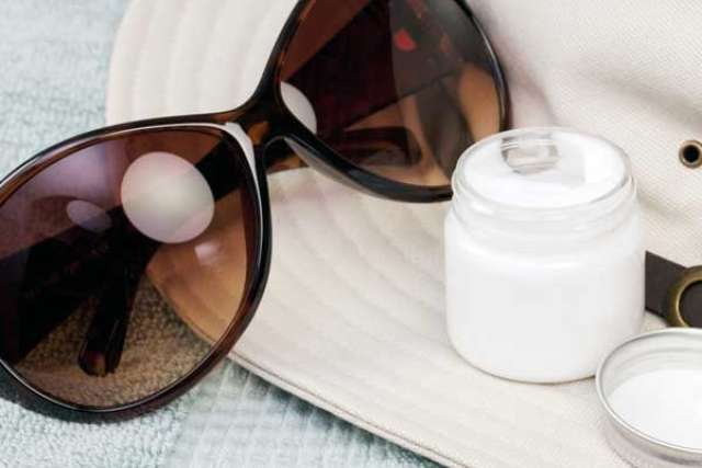 Brown oversized sunglasses on wide-brim hat beside open jar of cream
