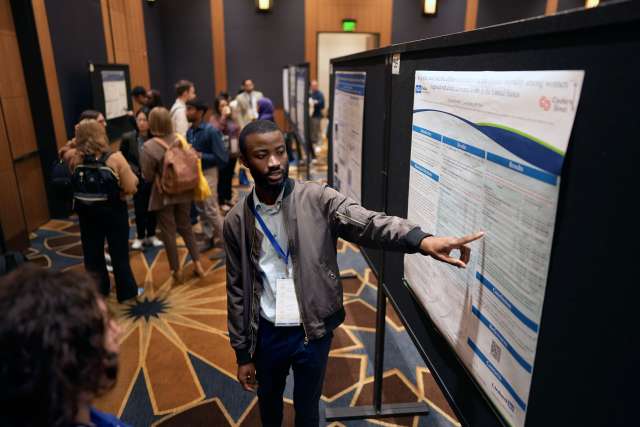 A young cancer researcher points at his poster