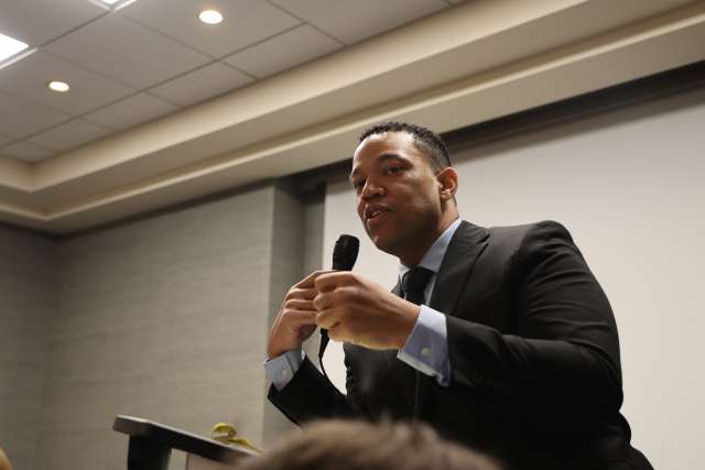 Man in suit speaking at podium, holding a microphone