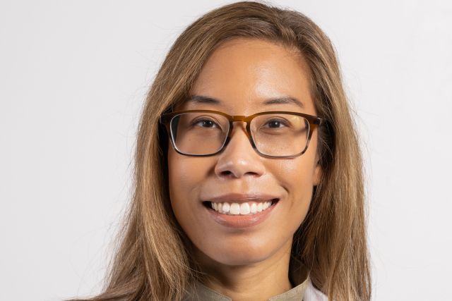 A medical professional wearing a lab coat with a neutral background.