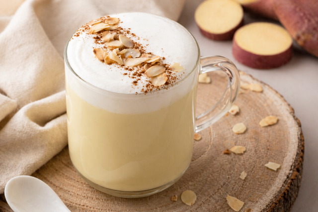 Glass mug with frothy latte on wooden board beside sliced sweet potatoes