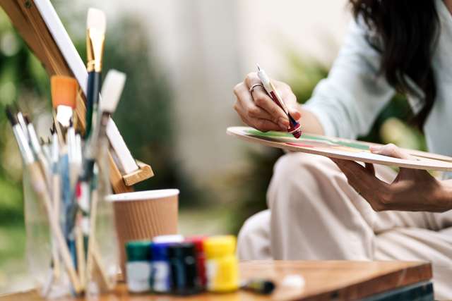 woman painting with brushes and jars of paint nearby