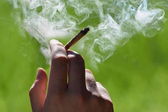 Hand holding lit joint with smoke against green background
