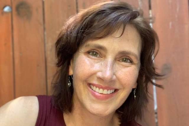 Tara Paul smiling in front of a wood panel fence