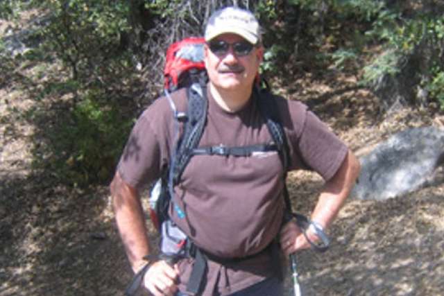 Mark Felling in hiking gear with red helmet and backpack on a sunlit rocky trail