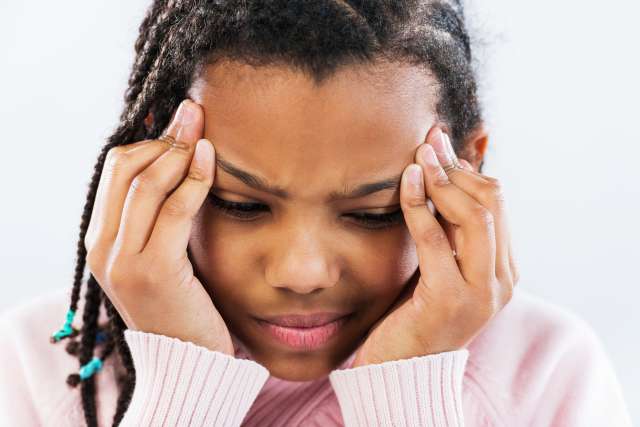 A young girl with a headache touches the sides of her forehead.