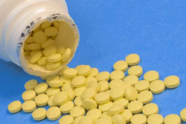 White bottle tipped over with numerous small yellow tablets scattered on a blue surface.