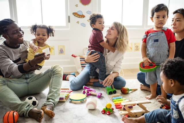 Daycare caregivers and toddlers sitting on floor playing with toys.