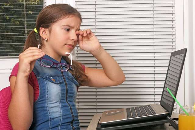 Girl rubbing her eyes with glasses at a laptop