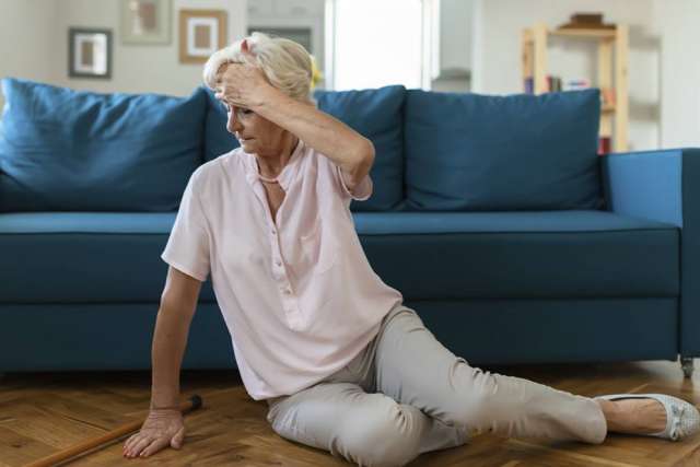 Older woman sitting on floor beside sofa holding her head