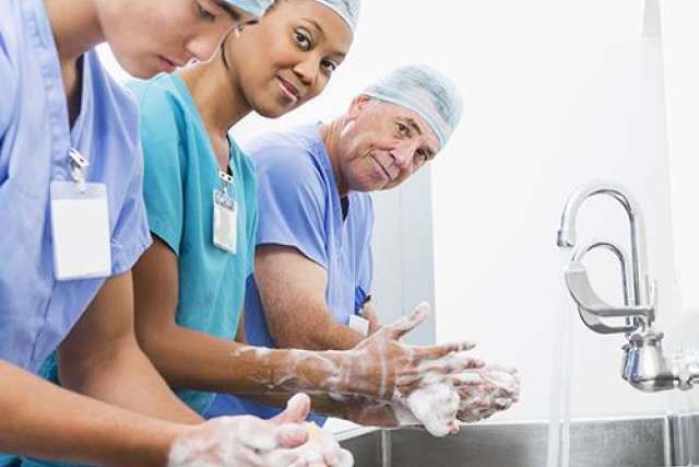 Medical staff in scrubs washing hands at a stainless steel sink with running water, preparing for a procedure.