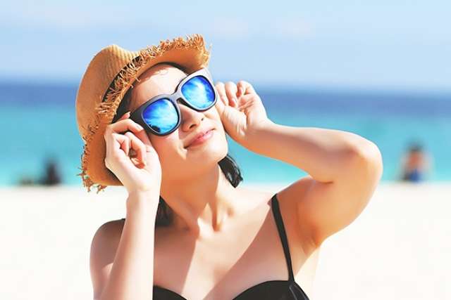 Woman at beach adjusting mirrored sunglasses