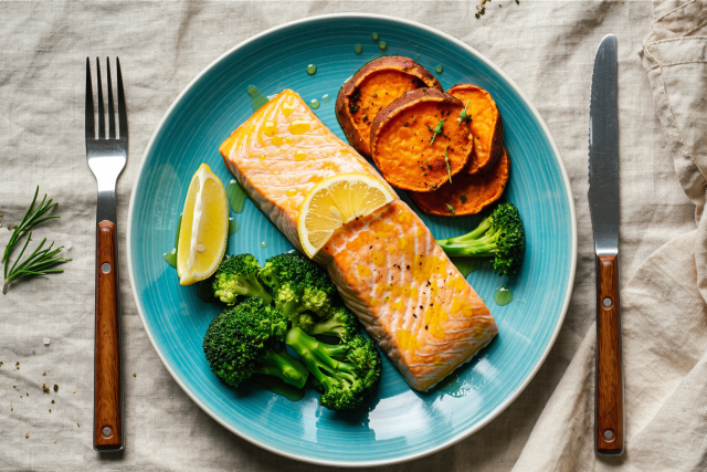 Cooked salmon fillet with broccoli, roasted squash and lemon wedge on blue plate.