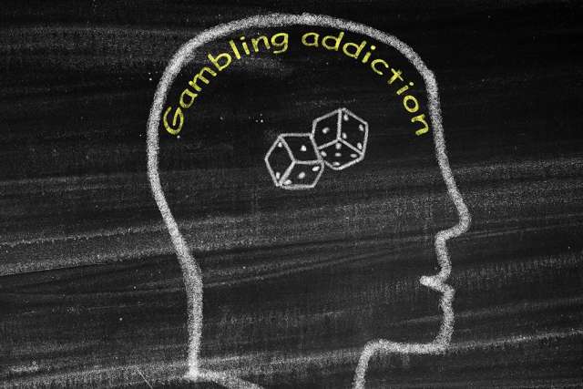 Chalk drawing of a human head outline with dice inside and the words “Gambling addiction” written above.