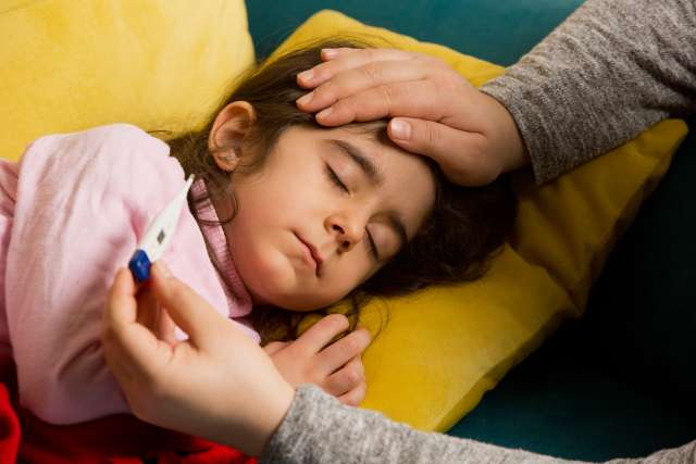 A caregiver checks the temperature of a child resting on a couch.