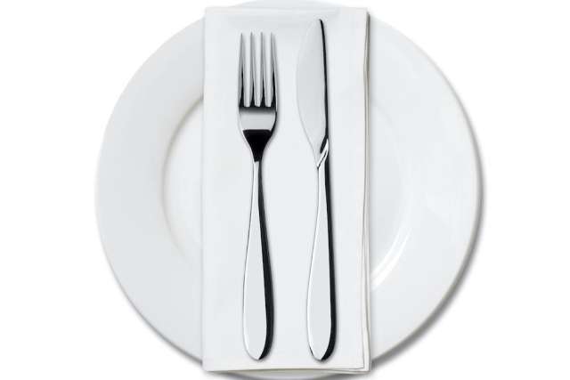 A knife and fork arranged on a napkin atop a white plate.