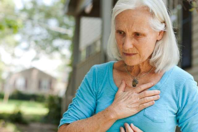 Older woman clutching chest on front porch