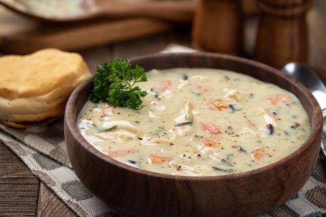 Creamy chicken soup in a wooden bowl, garnished with parsley, beside a biscuit.