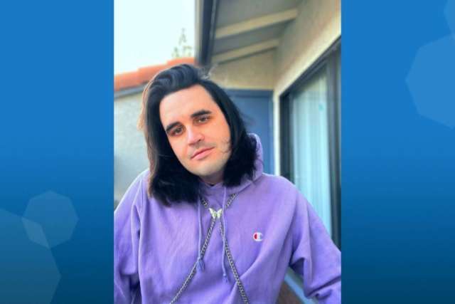 A person wearing a purple hoodie stands outdoors near a building.