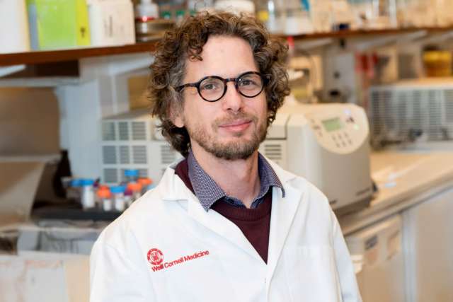 Dr. Dan Landau wearing a lab coat and glasses in a laboratory