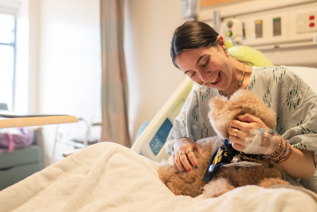 Hospital patient sits in a bed, smiling and holding a therapy dog.