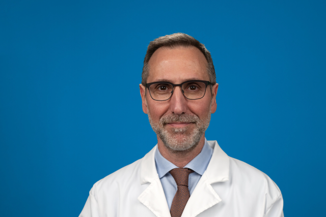 Individual with blurred face wearing white lab coat and tie against blue background.
