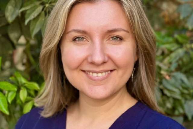 Portrait of Olena Svetlov wearing blue scrubs and standing in front of foliage.