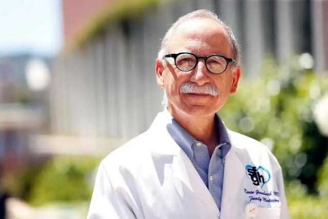 Person in white lab coat standing outdoors near a building