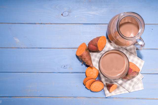 A pitcher and glass of chocolate beverage with sweet potatoes on a checkered cloth.