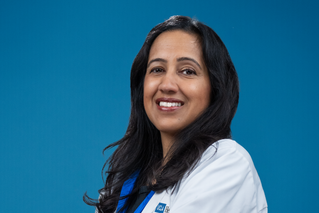 Dr Rajita Patil headshot, standing in front of a blue background, wearing her lab coat.