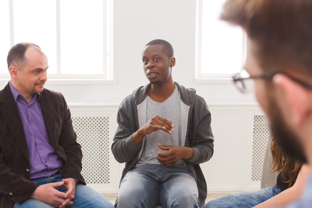 Three men sitting in a circle engaged in a support group session.