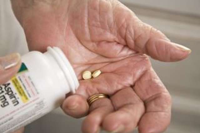 A person holds a bottle of pills in one hand and a single pill in the other, indicating medication use.