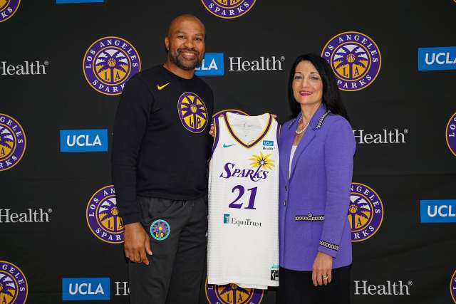 Johnese Spisso and Derek Fischer holding a Los Angeles Sparks jersey and smiling for a photo