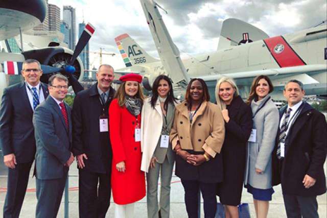 Group of eight people standing outside near aircraft, smiling at the camera.