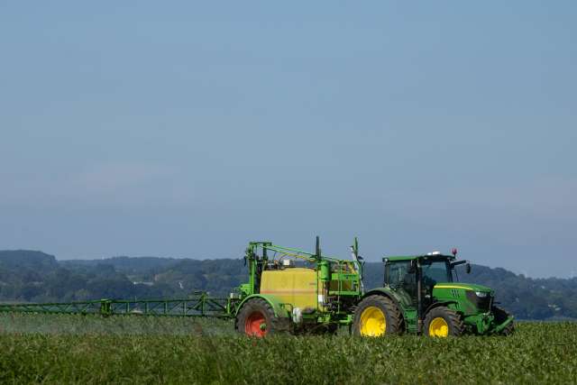 Green tractor spraying crops in a field under a clear blue sky.