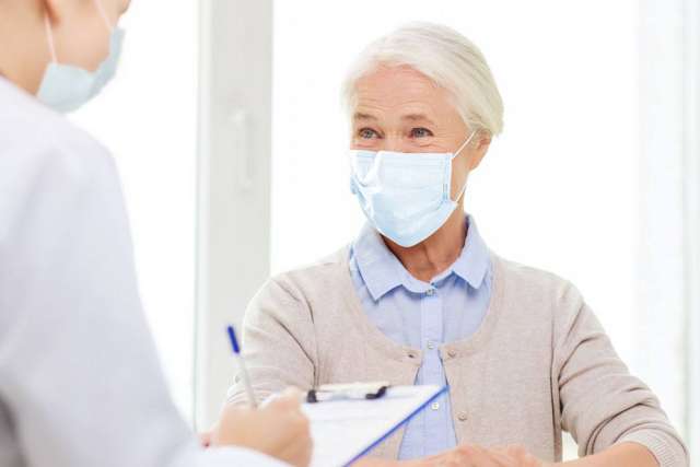 Older woman wearing mask speaking with masked clinician holding clipboard