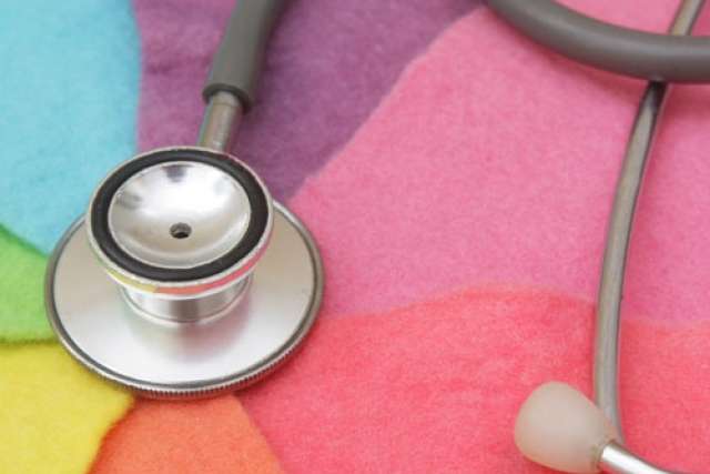 A close-up of a stethoscope's diaphragm and tubing resting on a brightly colored, textured background of pink, yellow, purple, and green fabric.