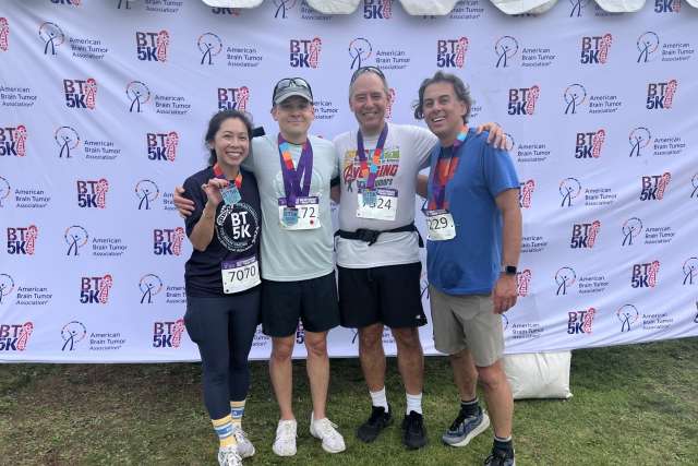 Four smiling runners wearing medals and race bibs in front of a sponsor backdrop